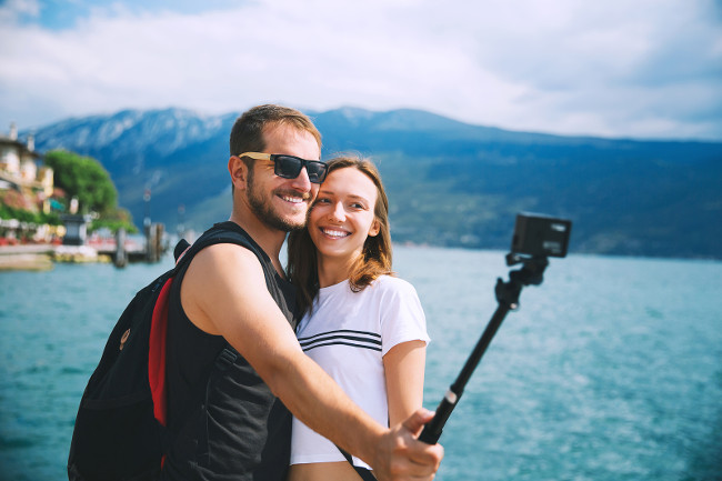 Tourist couple of lovers making selfie photo on motion camera at Lake Garda Italy Europe. Holidays and Travel Concept. Happy couple recording their trip with action camera.