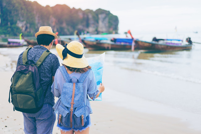 Young love couple traveler with backpack and hat looking map at the sea with long boat thailand background from Ao Nang Beach Krabi. Traveling in Krabi Thailand Traveler summer concept