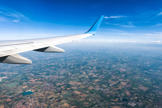 Wing of an airplane flying above villages or countryside. The plane's wing on the blue sky and earth background. Aerial panoramic view of motley land from airplane window. Travel concept.