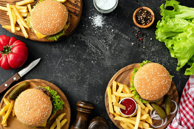 Burgers, hamburgers, french fries and fresh vegetables. BBQ party food. Dark background, top view and copy space for text. Summer barbecue concept