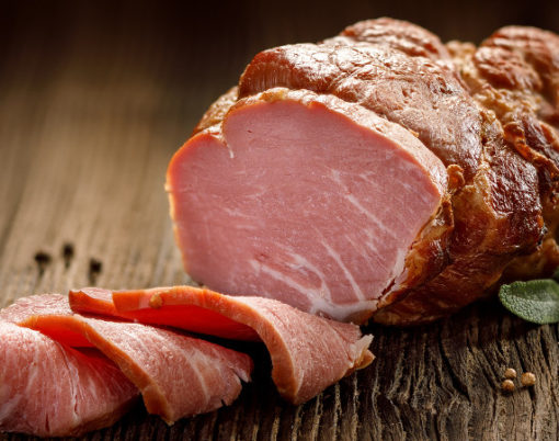 Sliced smoked gammon on a wooden table with addition of fresh herbs and aromatic spices. Natural product from organic farm, produced by traditional methods