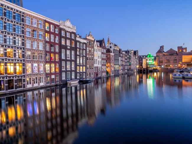 Amsterdam, Netherlands - July 18, 2018: Traditional canal houses on the Damrak at dusk in Amsterdam. Buildings on the canal are a form of traditional Dutch architecture which is now very popular.