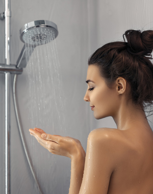 Beautiful girl standing at the shower. Portrait of happy mixed race Caucasian Asian slim woman taking shower at home. Skincare, spa and aromatherapy concept. Side view. Female enjoying water under a shower jet