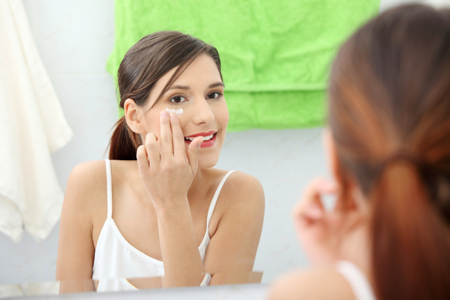 Beautiful woman applying cream on face at bathroom