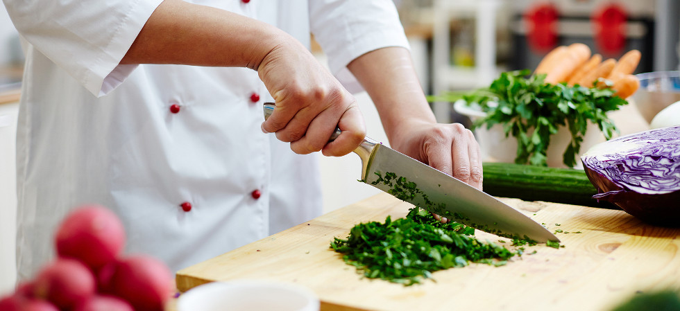 Chef cutting greenery with sharp professional knife on wooden board while cooking in the kitchen