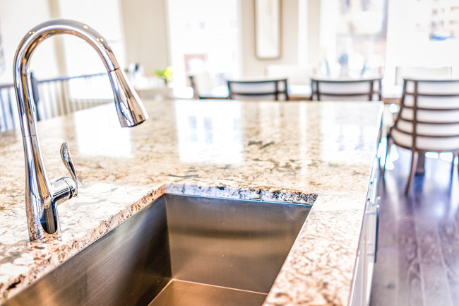 New modern faucet and kitchen room sink closeup with island and granite countertops in model house home apartment