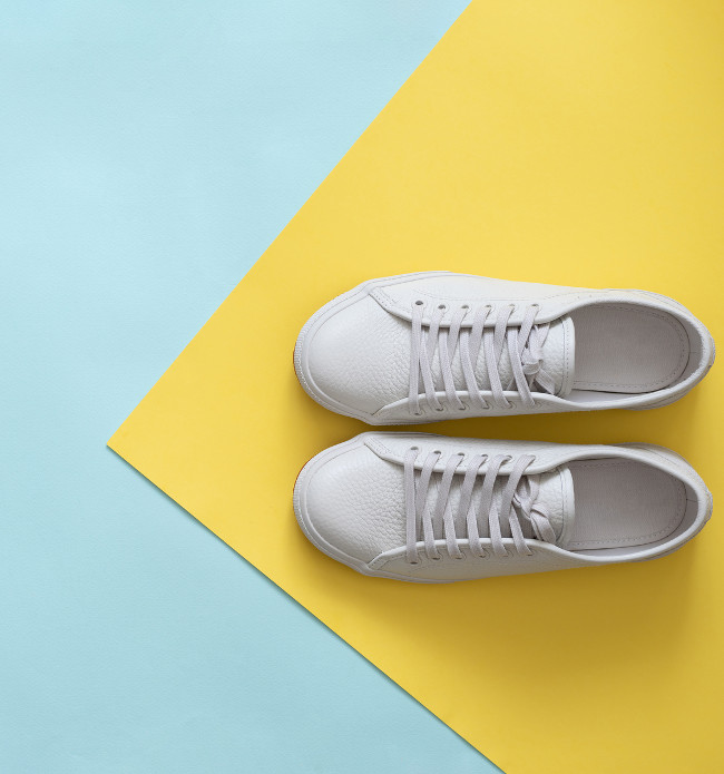 White leather sneakers on blue and yellow background. Pair of fashion trendy white sport shoes or sneakers with copy space for text on colorful background. Overhead shot of new white sneakers.Flat lay