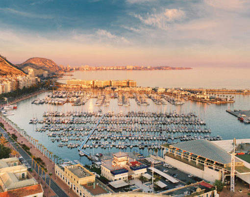 Aerial photography drone view Alicante cityscape above panorama main landmark in city center Santa Barbara castle on the Mount Benacantil moored yachts in the harbour Mediterranean sea at sundown, busy road along seaside, copy space. Spain