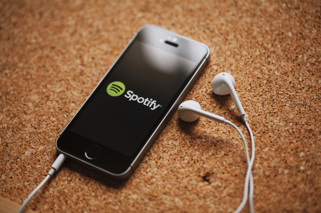 MALAGA, SPAIN - MARCH 5, 2018: Smart phone with Spotify logo in the screen and white earphones, placed on a cork panel.