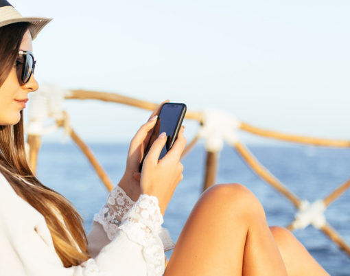 Portrait of young woman lying on a sunbed with phone in the hands on a sea background