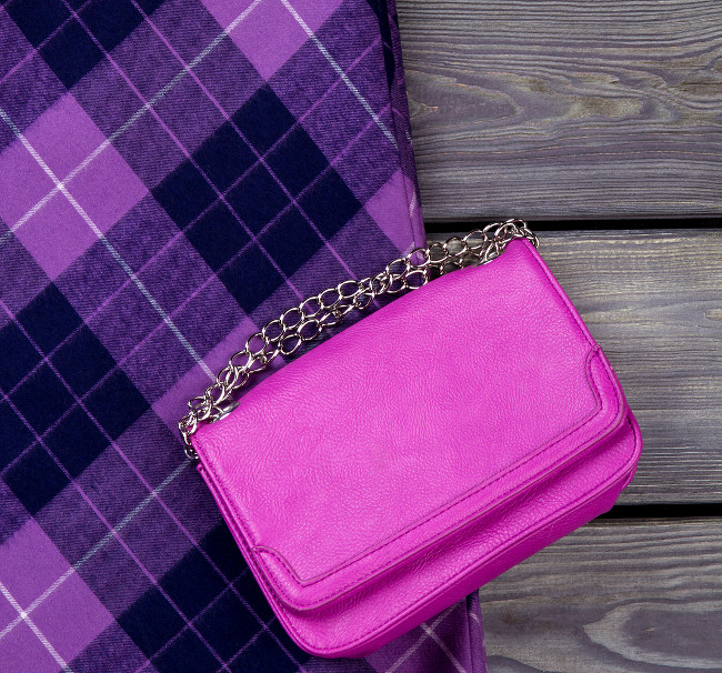 Top view purple handbag and checkered skirt. Grey wooden surface background.