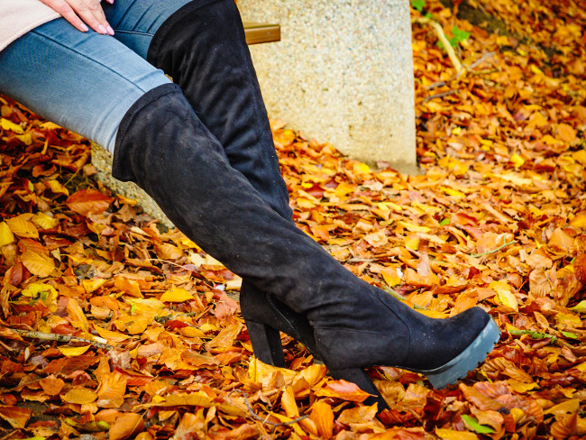 Woman wearing long black heeled knee high boots and jeans. Autumn fashion, warm footwear boots.