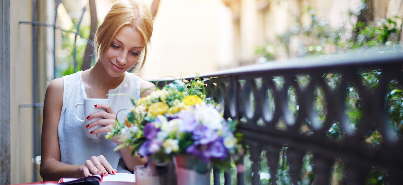 Pretty young woman reading book while sit at terrace table on her balcony, attractive young girl reading book while drinking coffee at sunny day sitting on balcony, sunny morning on beautiful balcony