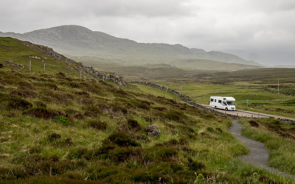 A view over the Highlands of Scotland with a motorhome parked up in a layby along the North Coast 500 route.