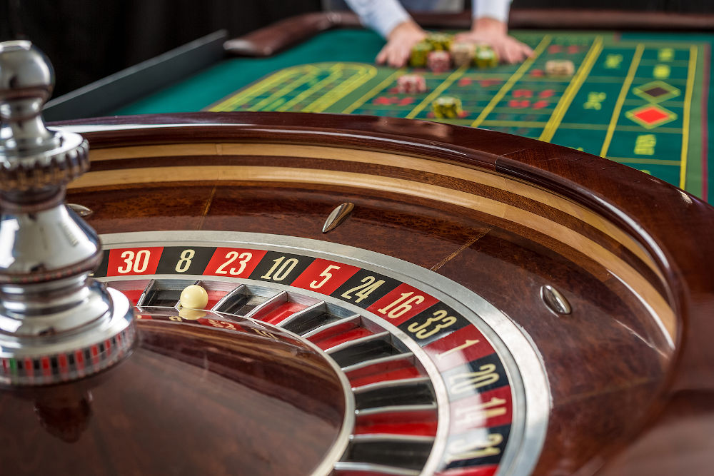 Close up view of Roulette and piles of gambling chips on a green table in casino. Man hand over casino chips on roulette table
