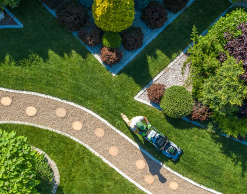 Gardener With Grass Mower Trimming Beautiful Backyard