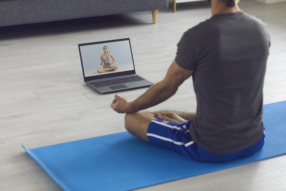 Man practicing yoga and watching an online fitness class 