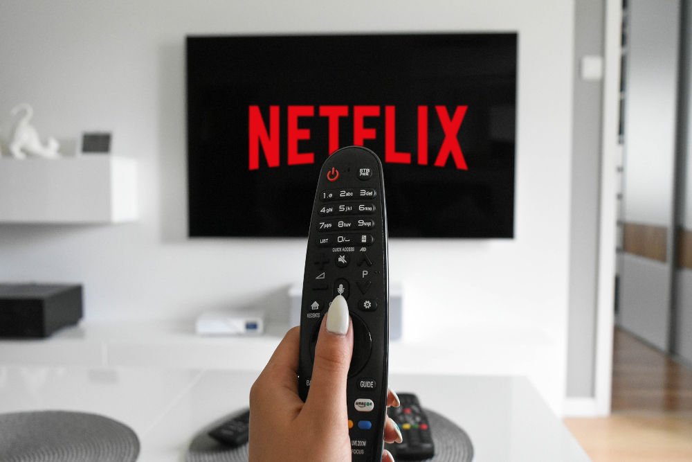 Netflix on a TV screen and a woman holding a remote