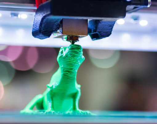 Print head of 3D printer machine printing plastic model of green toy lizard at modern scifi technology exhibition