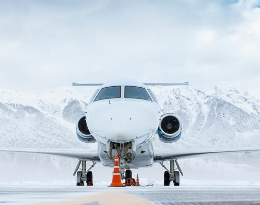 Front view of the white luxury corporate business jet on the winter airport apron on the background of high scenic mountains