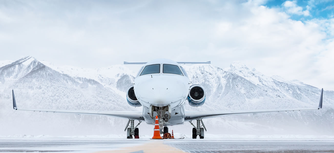 Front view of the white luxury corporate business jet on the winter airport apron on the background of high scenic mountains