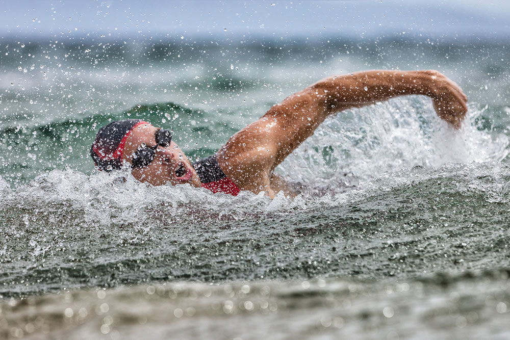 Triathlon swim tired swimmer swimming in ocean in wave and rain storm
