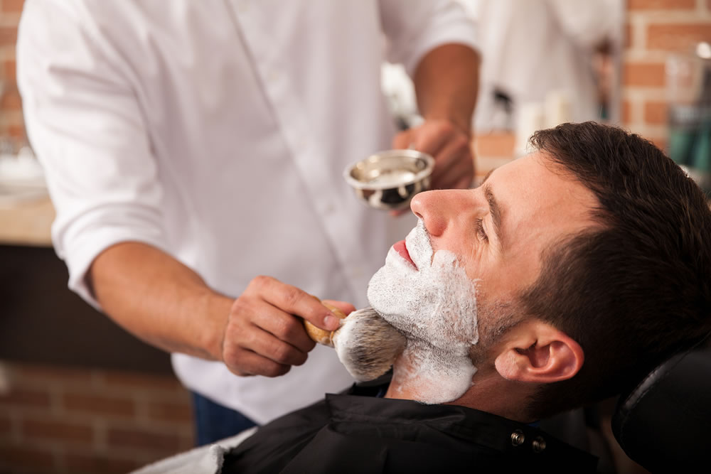 Barber putting some shaving cream on a client before shaving his beard in a barber shop