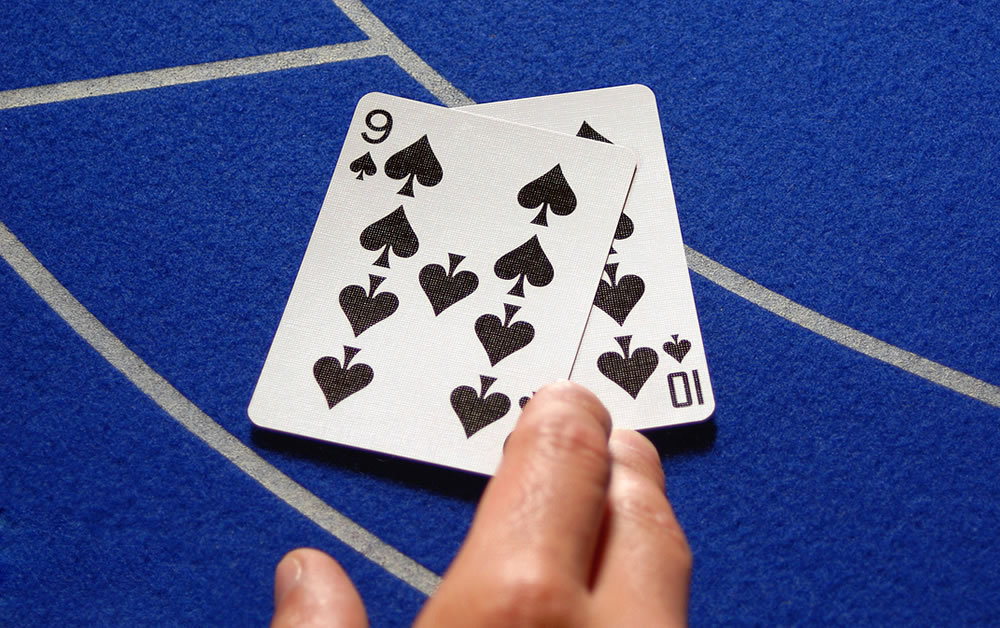 Two poker or baccarat cards on a Casino table. Male hand holding them