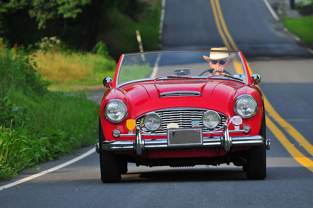 a frontal closeup of a senior classic sports car driver out on a country road