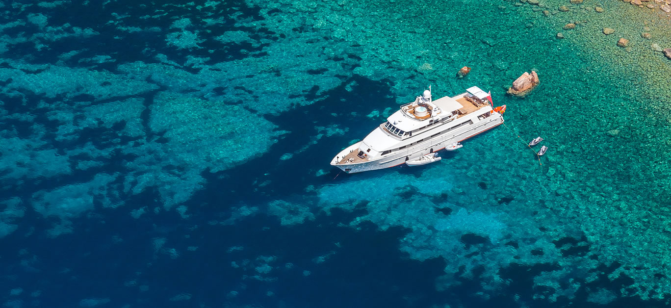 Luxury white pleasure yacht anchored near rocky coast of Corsica island birds eye view
