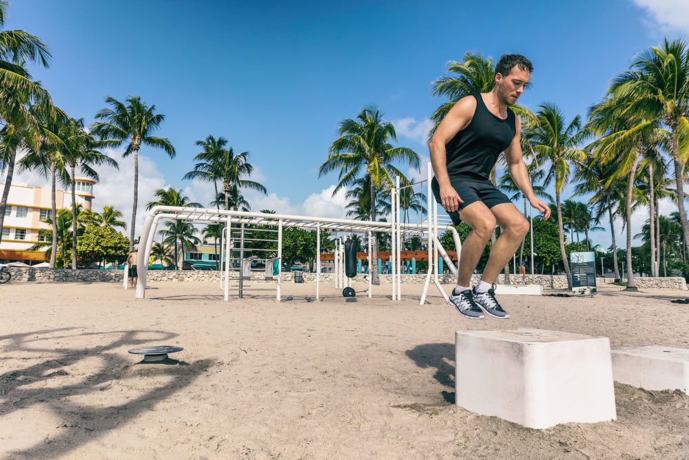 Training squat jumping on box in outdoor beach gym