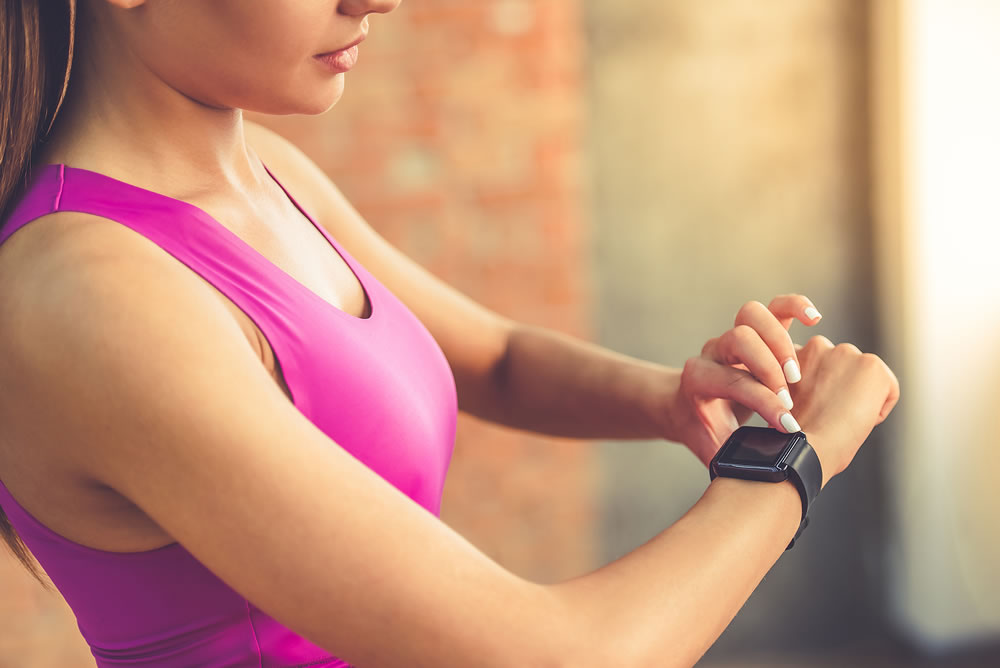 sports girl is switching on her fitbit before training while standing in fitness hall
