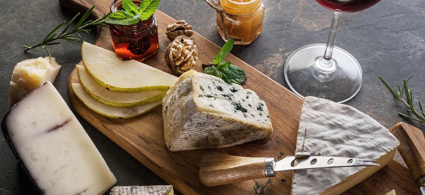 Cheese platter with organic cheeses, fruits, nuts and wine on stone background