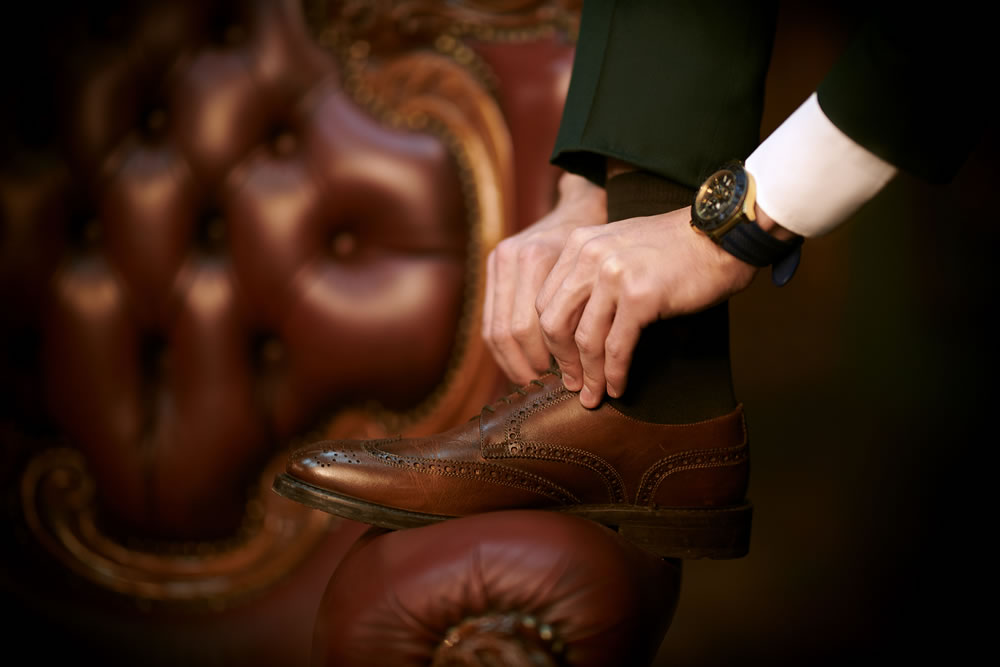 Close-up portrait of a man tying his shoelaces on brogues leaning his foot on the chair.