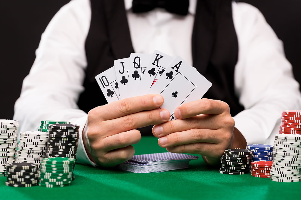 close up of poker player with playing cards and chips at green casino table