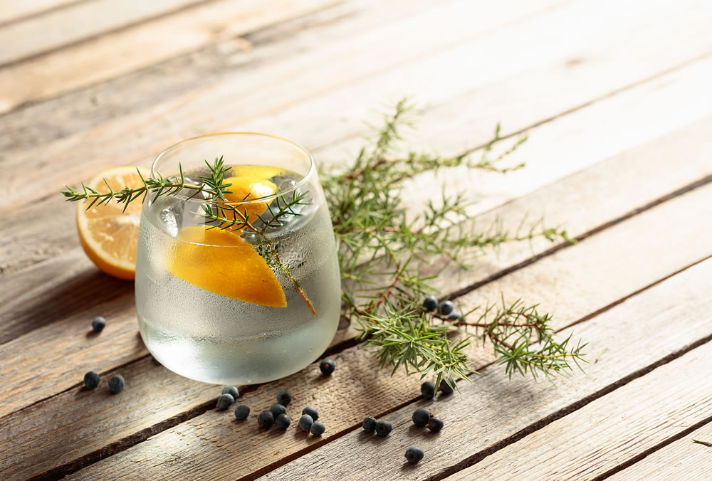 Gin tonic cocktail with lemon, juniper branch, and ice on rustic wooden table, copy space. Iced drink with lemon and juniper berries.