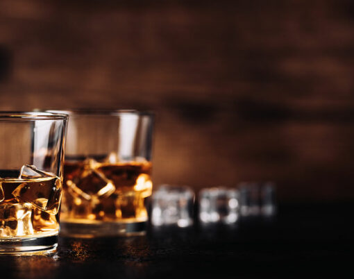 Whisky, whiskey, bourbon or cognac with ice cudes on black stone table and wood background