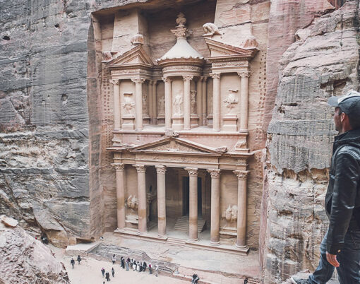 Aerial view of the Treasury with a hiker, solo traveler, young man tourist on a cliff after reaching the top, Al Khazneh in the ancient city of Petra, Jordan, UNESCO World Heritage Site
