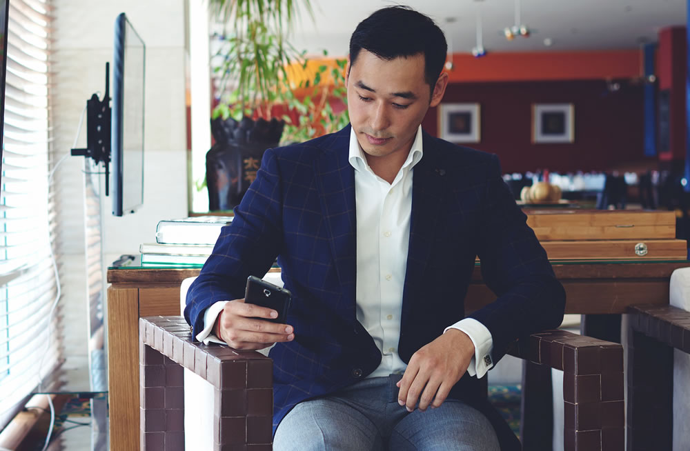 Portrait of handsome man dressed in luxury clothes chatting on his smart phone while sitting in cozy coffee shop inside