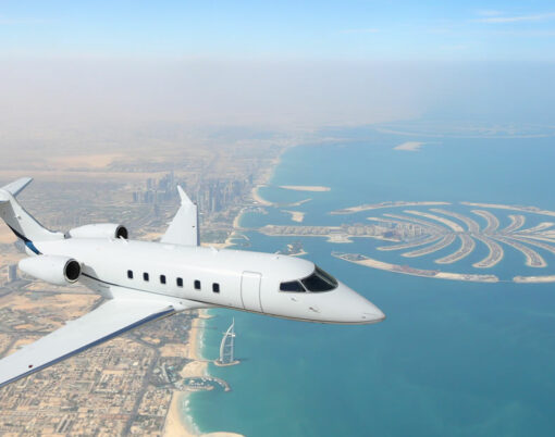 Business jet airplane flying over Dubai city and sea coastline.