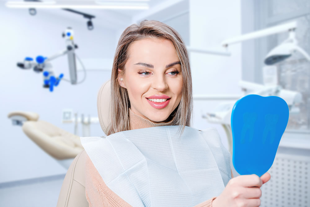 Happy attractive woman looking at her teeth in mirror. Satisfied patient of dental care or whitening for dental treatment.