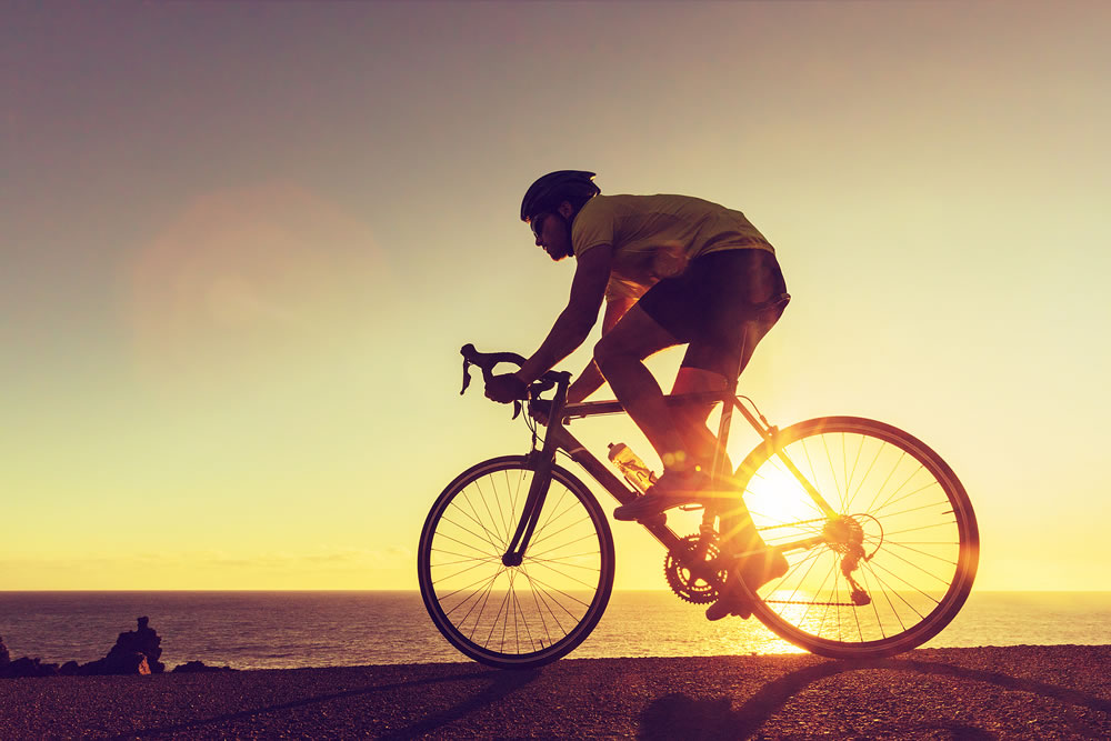Sports athlete silhouette. Road bike cyclist biking near ocean. Professional triathlete riding bike on an open road to the sunset. Active healthy man sport lifestyle.