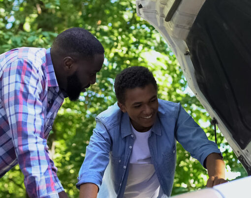 Black dad praising teenage son learning to repair car, family togetherness