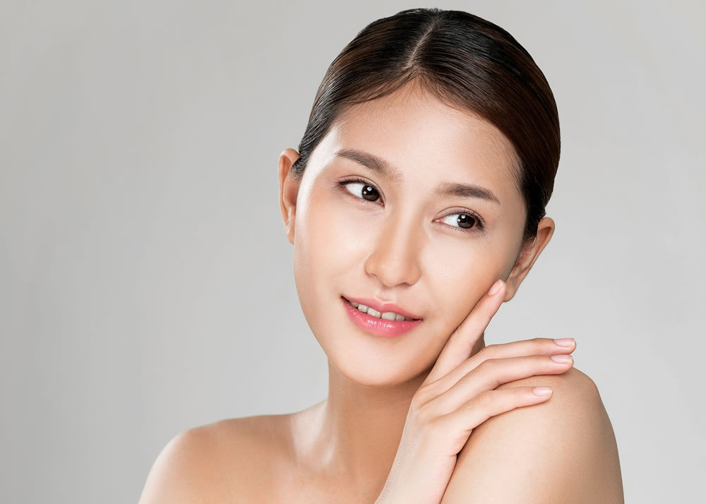 Closeup ardent young woman with healthy clear skin and soft makeup looking at camera and posing beauty gesture
