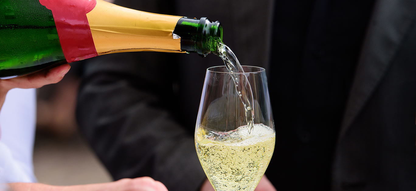 closeup of a champagne bottle pooring champagne into a champagne flute against a blurred person at a party