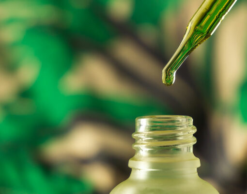 Dropping essential oil into glass bottle on blurred green background