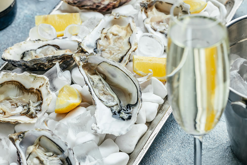 Fresh oysters with champagne on metal tray with lemon and ice