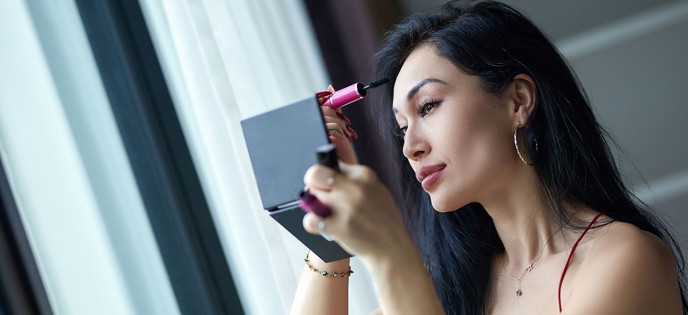 Close-up portrait of beautiful smiling woman doing evening make-up next to the window
