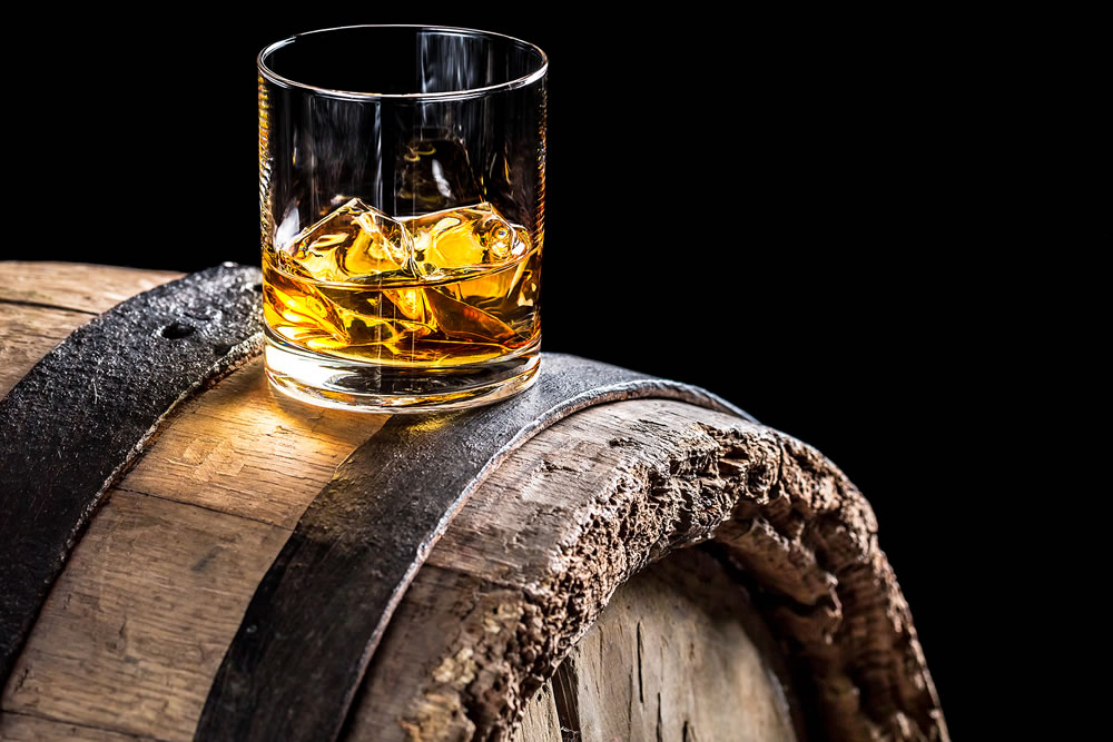 Glass of whisky with ice on old oak barrel