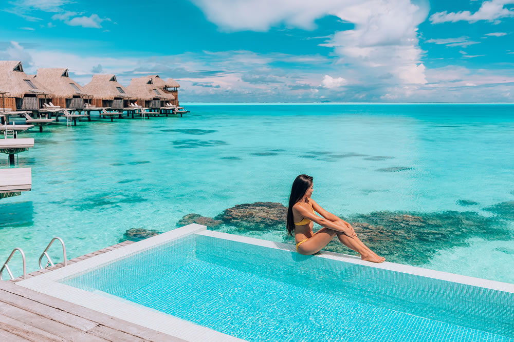 Luxury resort vacation destination idyllic overater bungalow villa woman relaxing by infinity pool